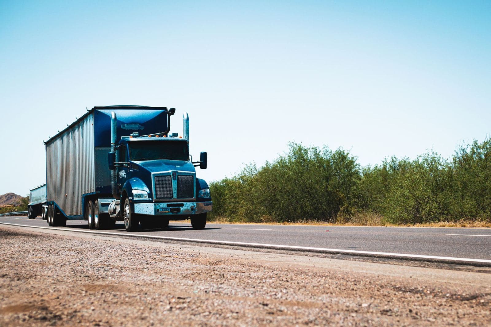 Blue semi truck pulling a dry van trailer down a highway
